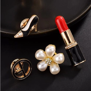 Detailed view of four fashion brooches including high heels and pearls on a black tray