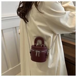 Détail du mini sac cylindre bordeaux avec chaîne argentée porté sur un trench beige