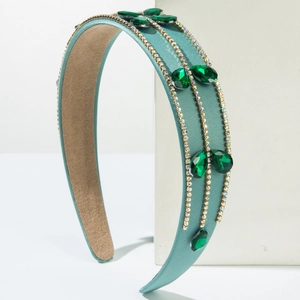 Teal satin baroque headband with emerald rhinestones on a geometric white stand