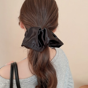 Close-up of a large black satin scrunchie styled in hair against a beige background
