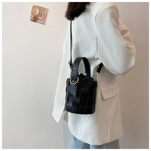 Detail of a black woven bucket bag with golden hardware and hand ring held by model