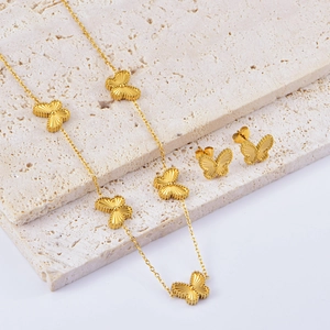 Golden double-sided embossed butterfly necklace and earrings set on stone display