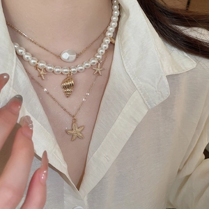 Detail view of a triple-layered necklace featuring a gold starfish and pearl pendants