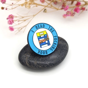 Insigne rond en émail pour livres avec bordure bleue sur un galet sur fond blanc