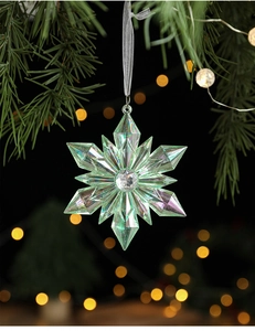 Iridescent acrylic snowflake ornament with gemstone center hanging on a pine tree branch