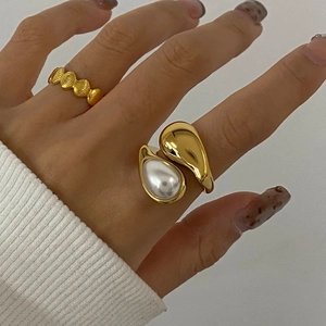 Dettaglio di anello a goccia dorato con perla e fascia testurizzata indossato su dito