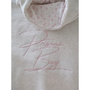 Détail des lettres brodées roses et doublure florale sur le sweat gris en coton