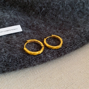 Detailed view of gold hoop earrings with textured geometric facets on a soft fabric surface