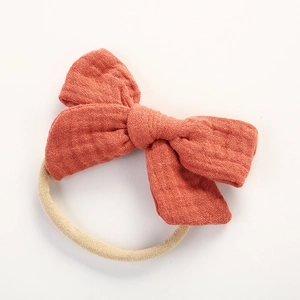 Détail d'un nœud en coton mousseline rouge brique avec texture douce sur un élastique beige