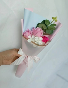 Close-up of hand-held pink soap rose bouquet with artificial leaves and ribbon