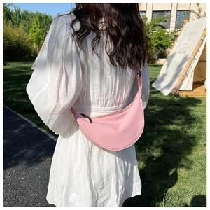 Pink nylon crescent crossbody bag worn by a model in a sunlit outdoor grassy setting