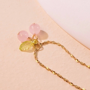 Detailed view of sweet cherry necklace with pink beads and green leaves on gold chain