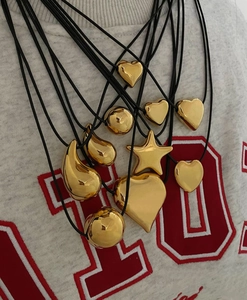 Macro view of polished gold-finished heart, star, and bean pendants on black wax cords
