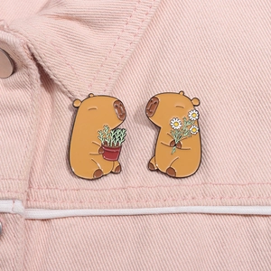 Macro detail of capybara enamel pins with daisy and plant on pink denim fabric