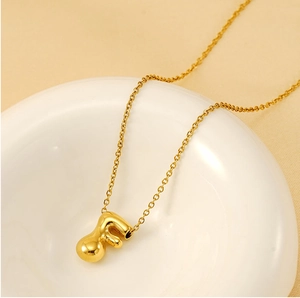 Detailed close-up of 18K gold letter F bubble pendant on a chain in a ceramic bowl