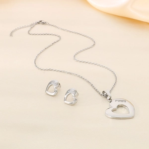 Close-up of silver hollow heart pendant and matching stud earrings on beige silk fabric