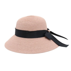 Detail of pink straw sun hat with wide brim featuring a decorative large black bow ribbon