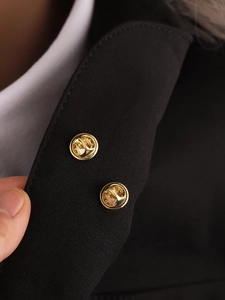 Macro shot of two golden metal butterfly clasp pins on a black blazer lapel with white shirt