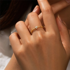 Close-up of a minimalist gold floral ring with four clear crystals on a model's finger
