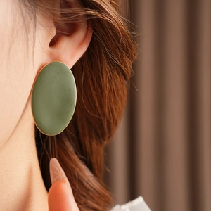 Dettaglio di un grande orecchino ovale verde oliva con bordo dorato su modella