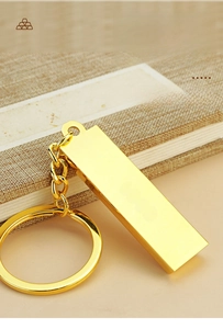 Polished gold bar keychain with metal link ring displayed on a textured fabric book cover