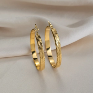 Detail of 18K gold-plated hoop earrings with herringbone texture on white silk fabric