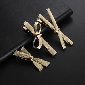 Close-up of golden metal bow hair clips with textured finish on black leather background
