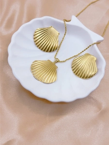 Detailed view of golden shell pendant necklace and earrings set on a white shell dish