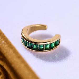 Close-up of 18K gold-plated ear clip with vibrant green baguette zircon on soft fabric