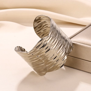Macro shot of wide textured gold cuff bracelet with modern rippled surface on satin background