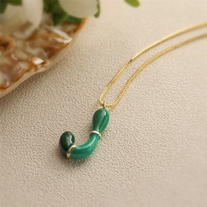 Dettaglio di una collana d'oro con un ciondolo a lettera J in smalto verde lucido
