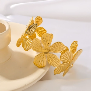 Polished gold textured flower bud cuff bracelet on a minimalist ceramic pedestal