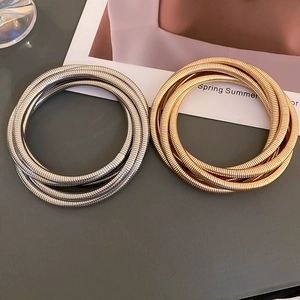 Detailed close-up of layered gold and silver snake bone bracelets with woven textures