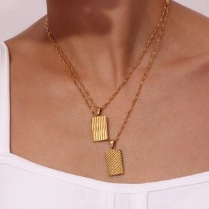 Macro detail of gold-plated double-layer necklace featuring rectangular embossed pendants