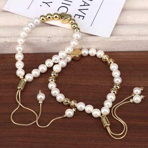 Adjustable pearl bead bracelet with gold heart charm and metallic beads on wood background