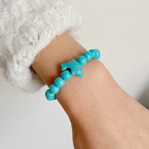 Blue turquoise beaded bracelet with central dolphin charm on wrist for a nautical look