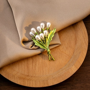 Close-up of golden leaf brooch with white pearls on elegant silk and wooden tray