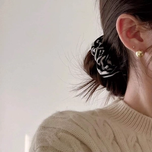 Close-up of a model wearing a gold spherical stud earring and a zebra print silk scrunchie
