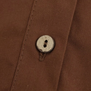 Close-up of a vintage button and textured brown poplin fabric on a casual fashion shirt