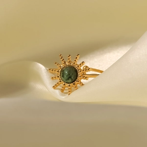 Gold sun-shaped steel ring with dark green turquoise stone on soft beige silk