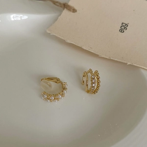 Detail of layered gold pearl ear cuff set with rhinestones on a white ceramic plate