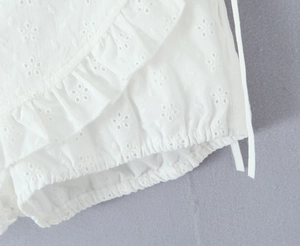 Close-up of white French style top with delicate embroidery and ruffled lace hem detail