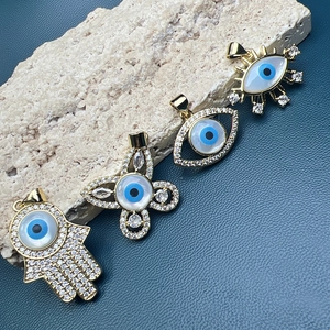 Macro shot of gold Hamsa Hand and Evil Eye charms with zircon on a natural stone base