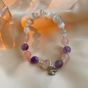 Detail of beaded bracelet with cat eye stones and butterfly charms on white silk fabric