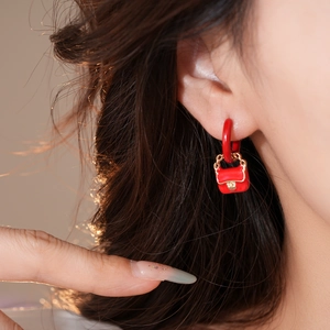 Detailed close-up of red handbag-shaped pendant earring with gold hardware detail