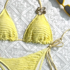 Detail of yellow bikini with ruffled texture and golden metal flower with pearl