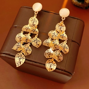 Detailed close-up of golden hollowed leaf tassel earrings on a brown jewelry box