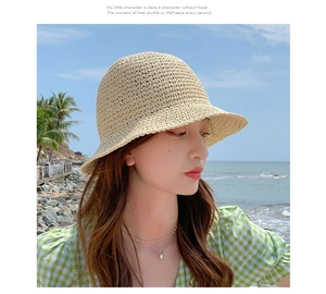Detail of a beige woven straw sun hat worn by a model in a coastal beach setting