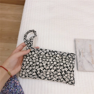 Détail d'un mini sac en tissu fleuri avec poignée sur un fond blanc texturé et sobre