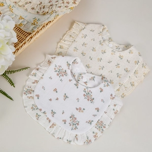 Close-up of baby floral cotton bibs with ruffled edges and snap fastener on beige background